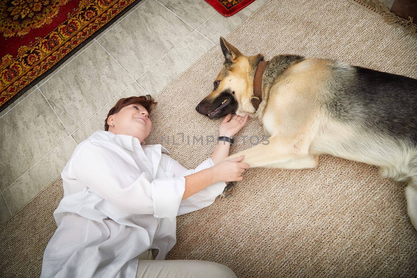 A woman in a cozy room smiles as she bonds with her German Shepherd dog during a relaxing moment.