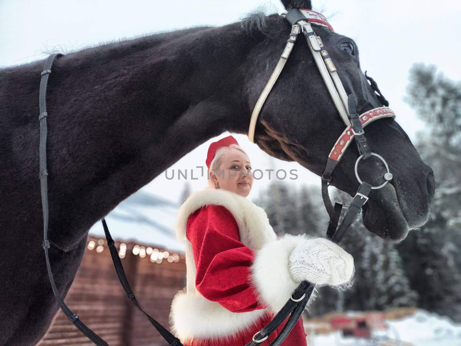 A beautiful Russian girl in a vibrant national dress poses with a horse, celebrating Maslenitsa in a winter setting.