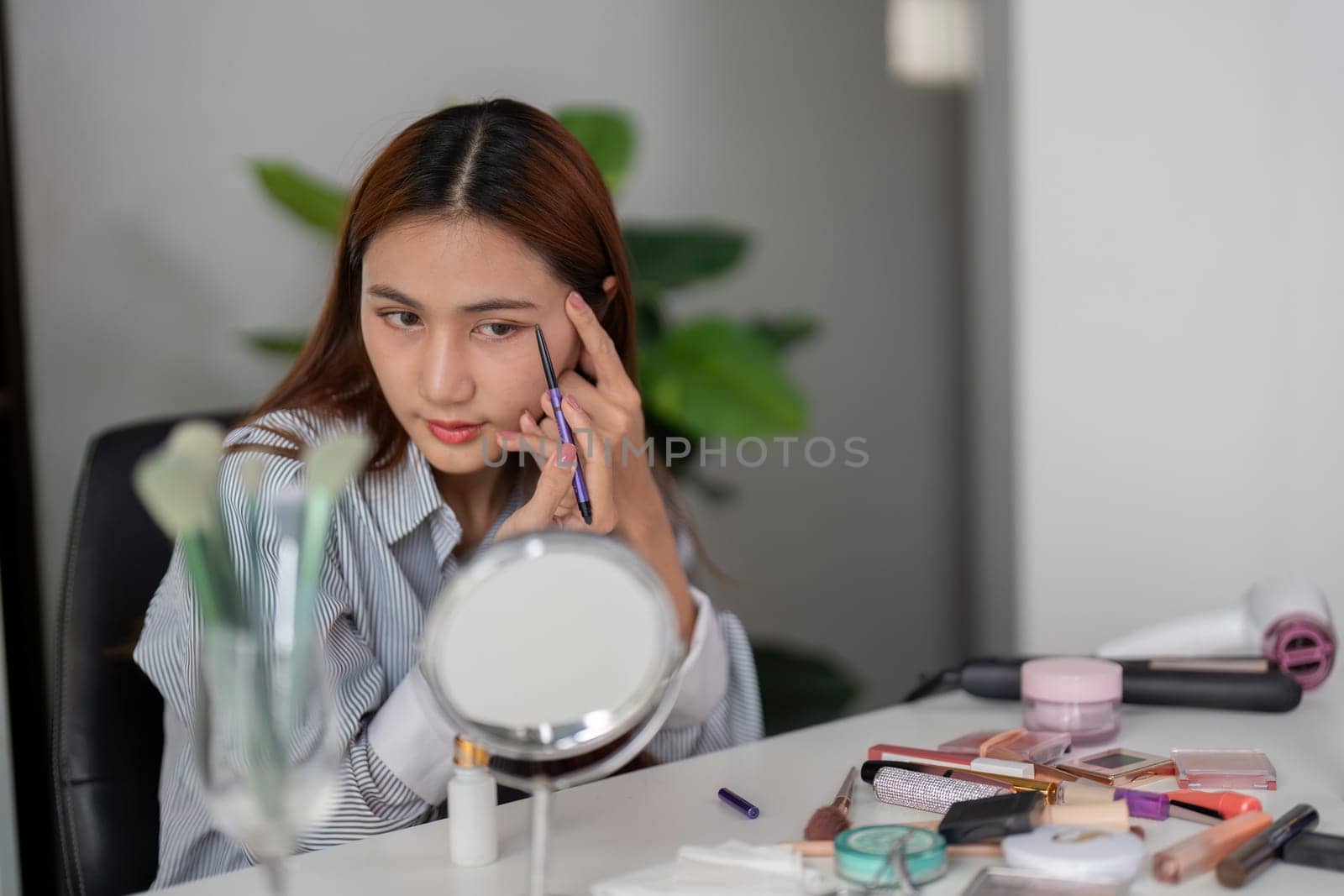 A woman meticulously shapes her eyebrows with an eyebrow pencil, focusing on detail for a stylish and defined look as part of her beauty regimen.