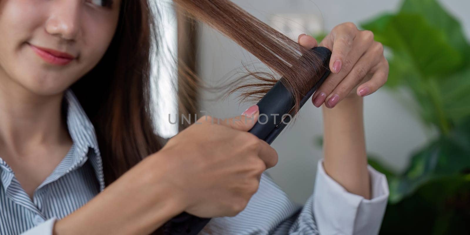 A young woman is styling her hair with a flat iron, focusing on achieving a smooth and polished look in her beauty routine.