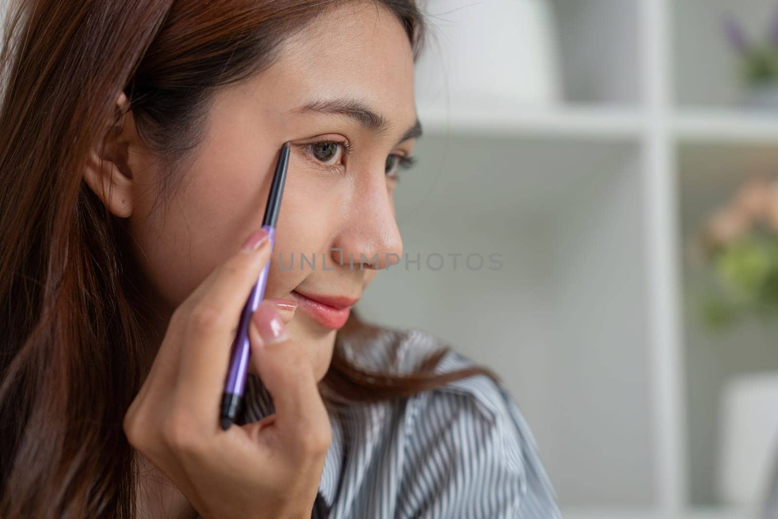 A young woman expertly applies eyeliner, focusing on enhancing her eyes as part of her makeup routine.