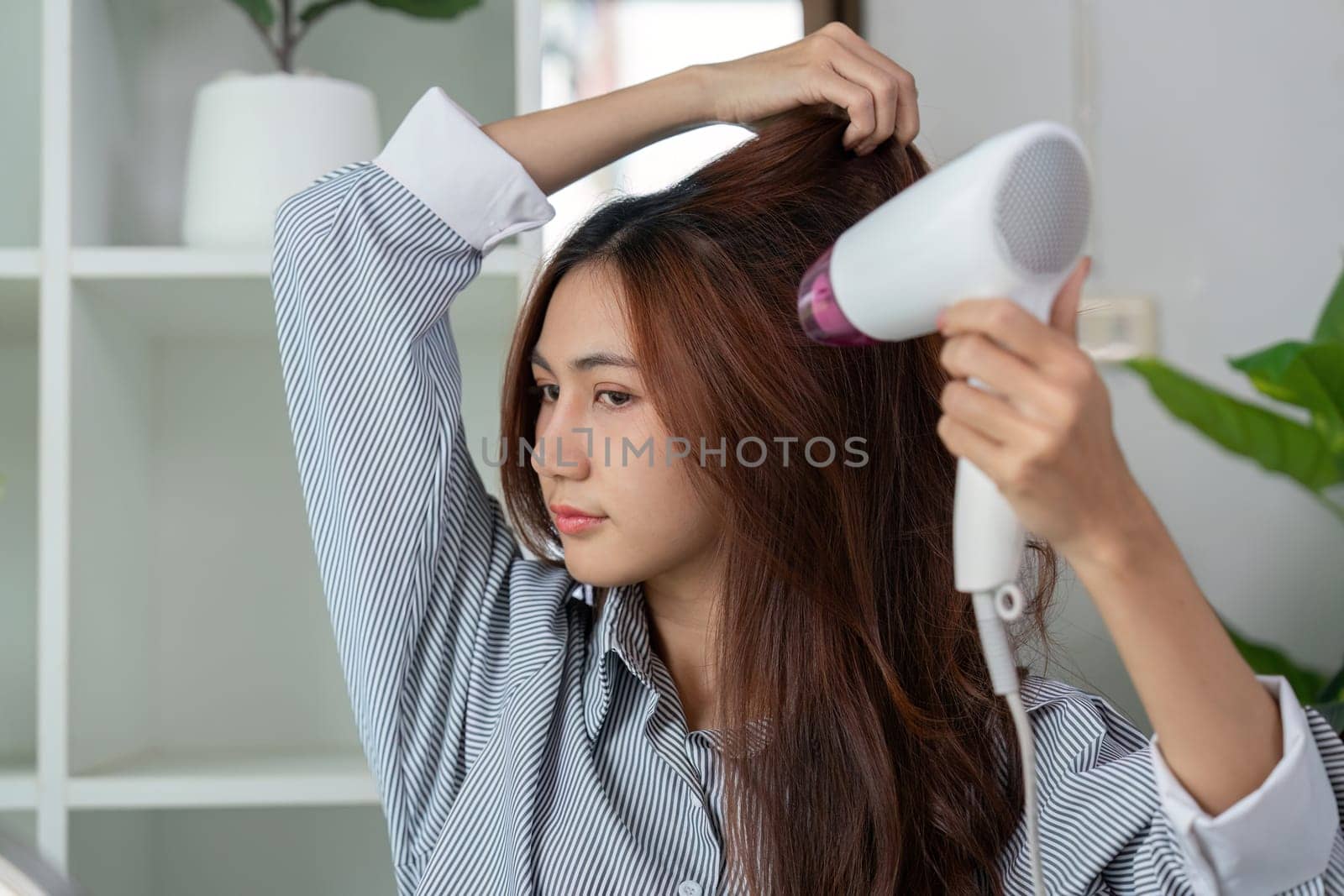 A young woman blow-dries her hair, using heat to create volume and a sleek finish as part of her daily beauty routine.