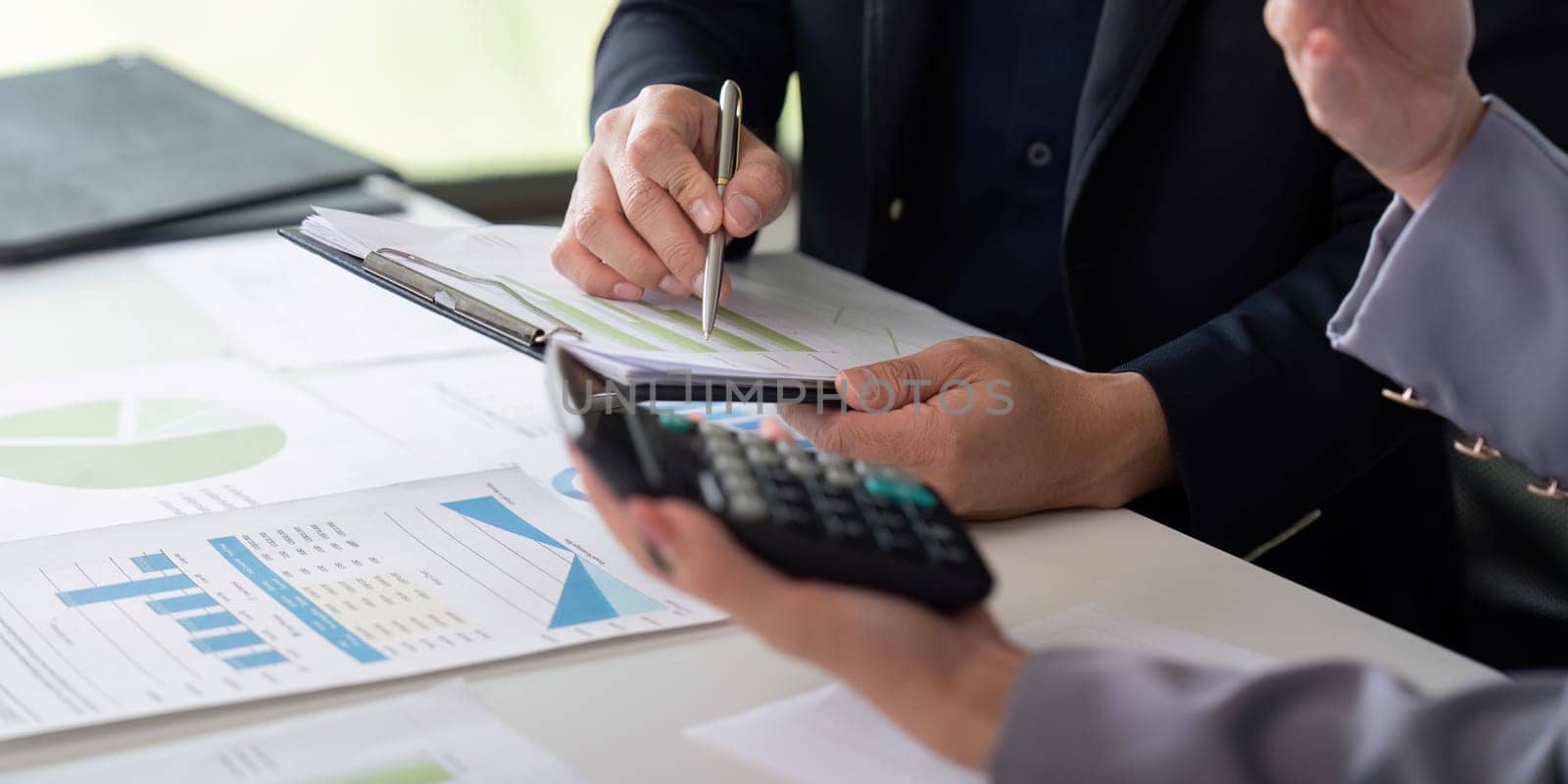 Two professionals engage in a detailed financial discussion, reviewing colorful graphs and notes while utilizing a calculator to enhance their analysis.