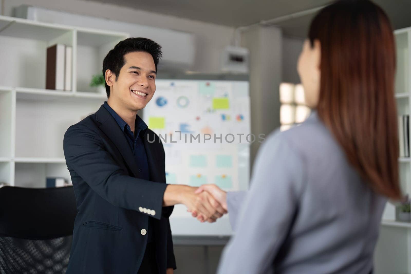 Two colleagues meet and shake hands in a contemporary workspace, symbolizing professionalism and collaboration in a corporate environment.