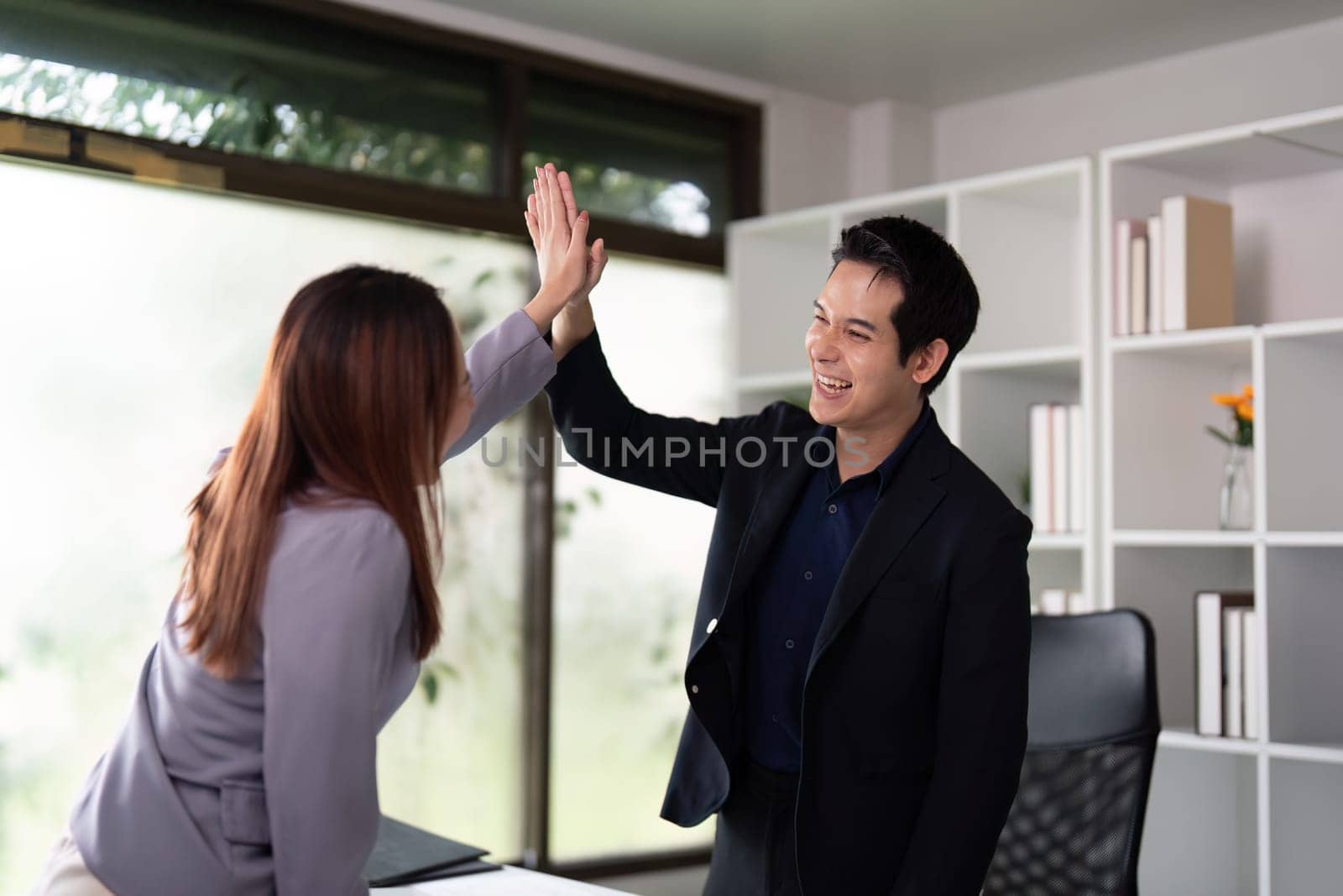 In a cheerful workspace, two professionals share a high-five, celebrating a collaborative effort, showcasing teamwork and positive energy.