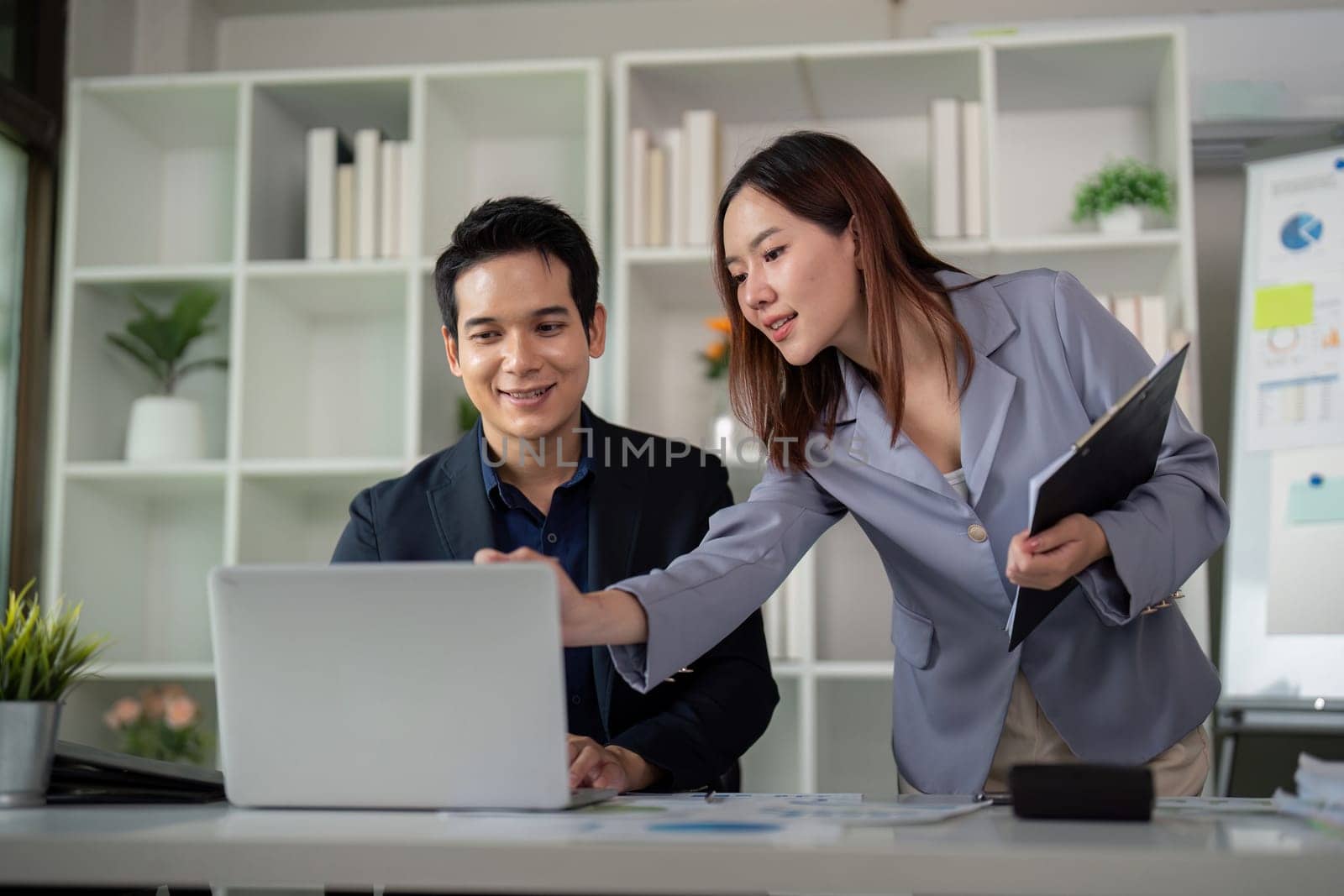 In a stylish office setting, two colleagues collaborate on a project using a laptop, highlighting their teamwork and shared ideas.