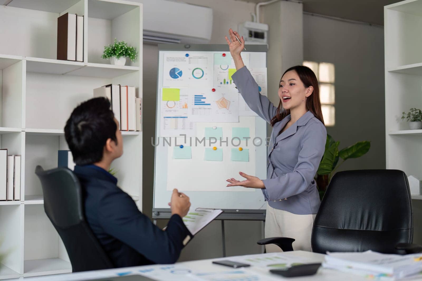 In a sleek office, a professional woman presents data and insights on a whiteboard, showcasing her communication skills and engaging her colleague in discussion.