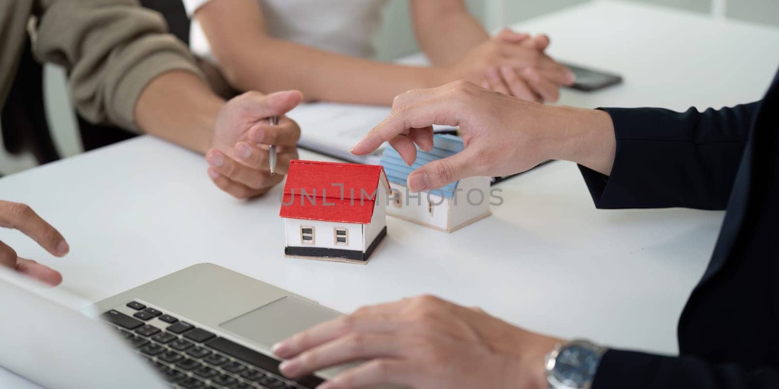 During a property consultation, a couple consults with their real estate agent, using a laptop and model homes to strategize their home buying decisions.
