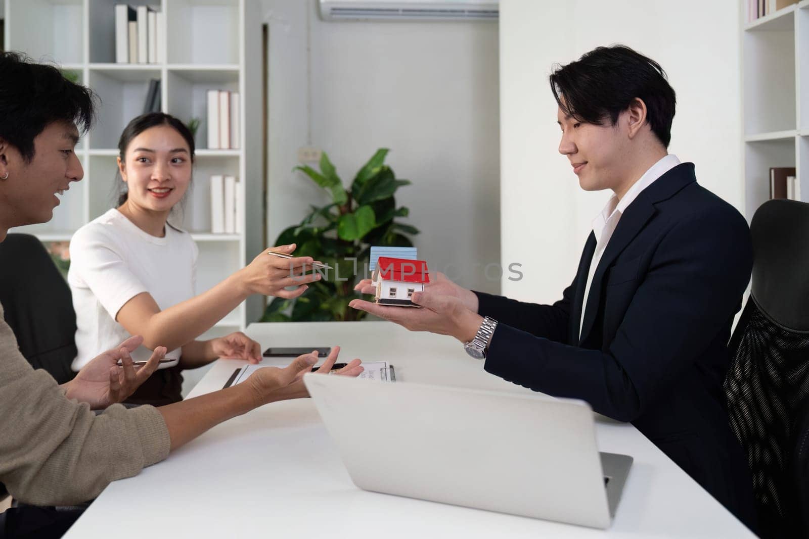 In a professional setting, a real estate agent shows models of houses to a couple, highlighting features while facilitating a fruitful discussion about their home buying needs.