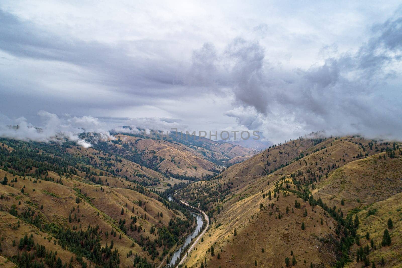 The sky is cloudy and the mountains are brown. The valley is filled with trees and the river is winding through it