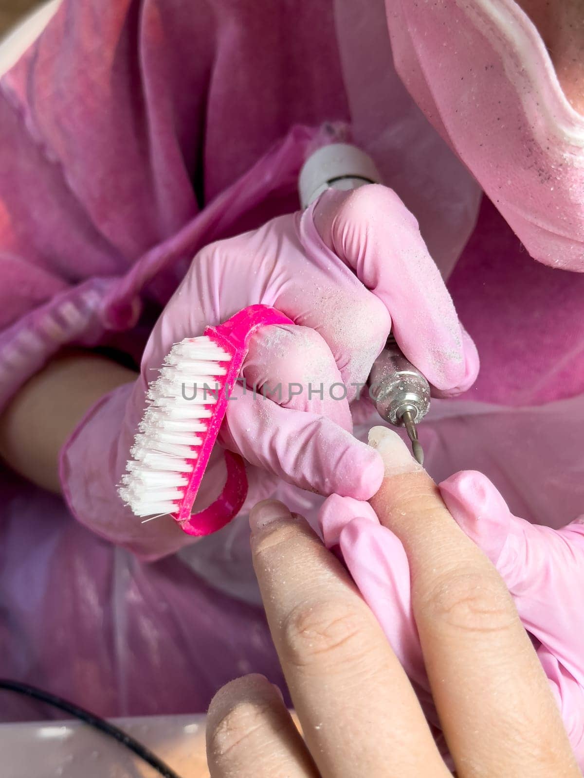 Close up of nail technician in pink gloves performing manicure on female hand.