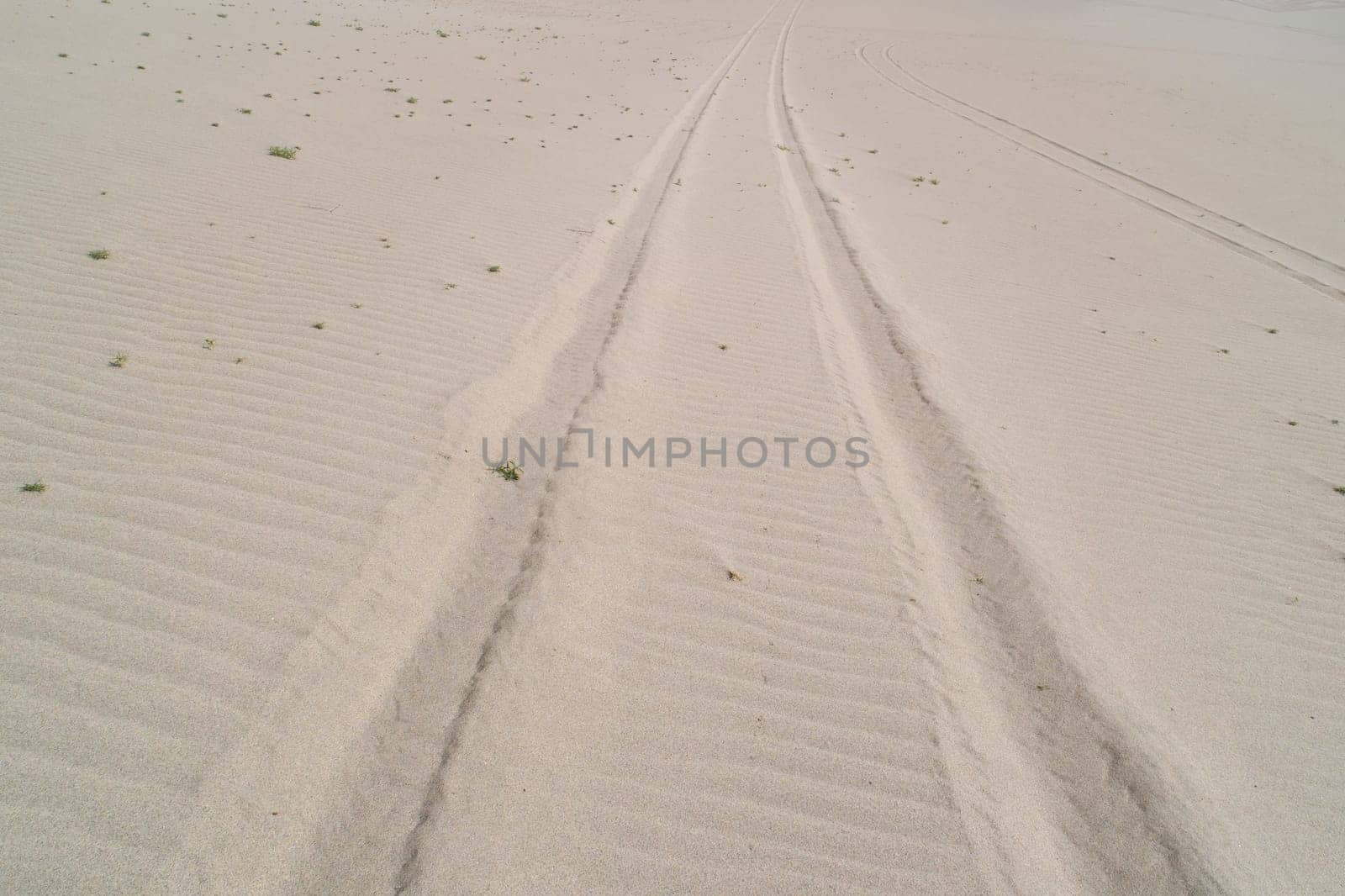 A sandy beach with a few footprints in the sand. The footprints are in a straight line, and the sand is very dry