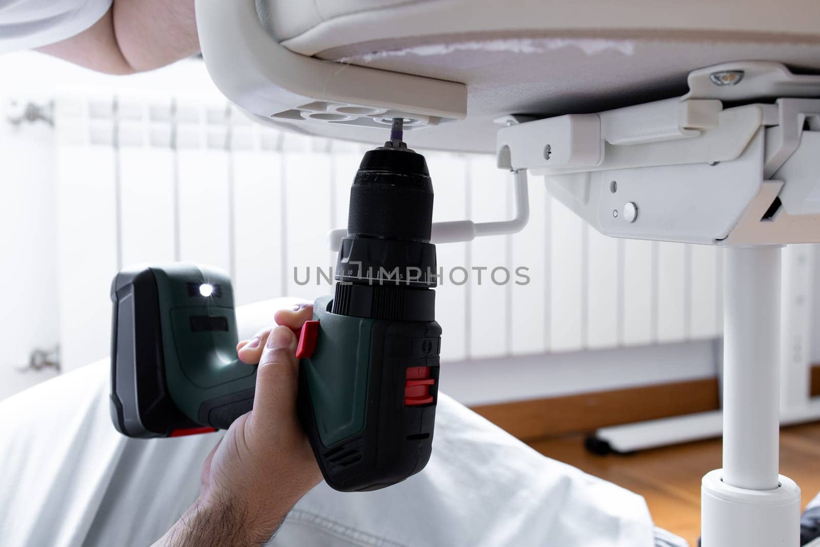 Male adult assembling furniture with electric drill indoors.