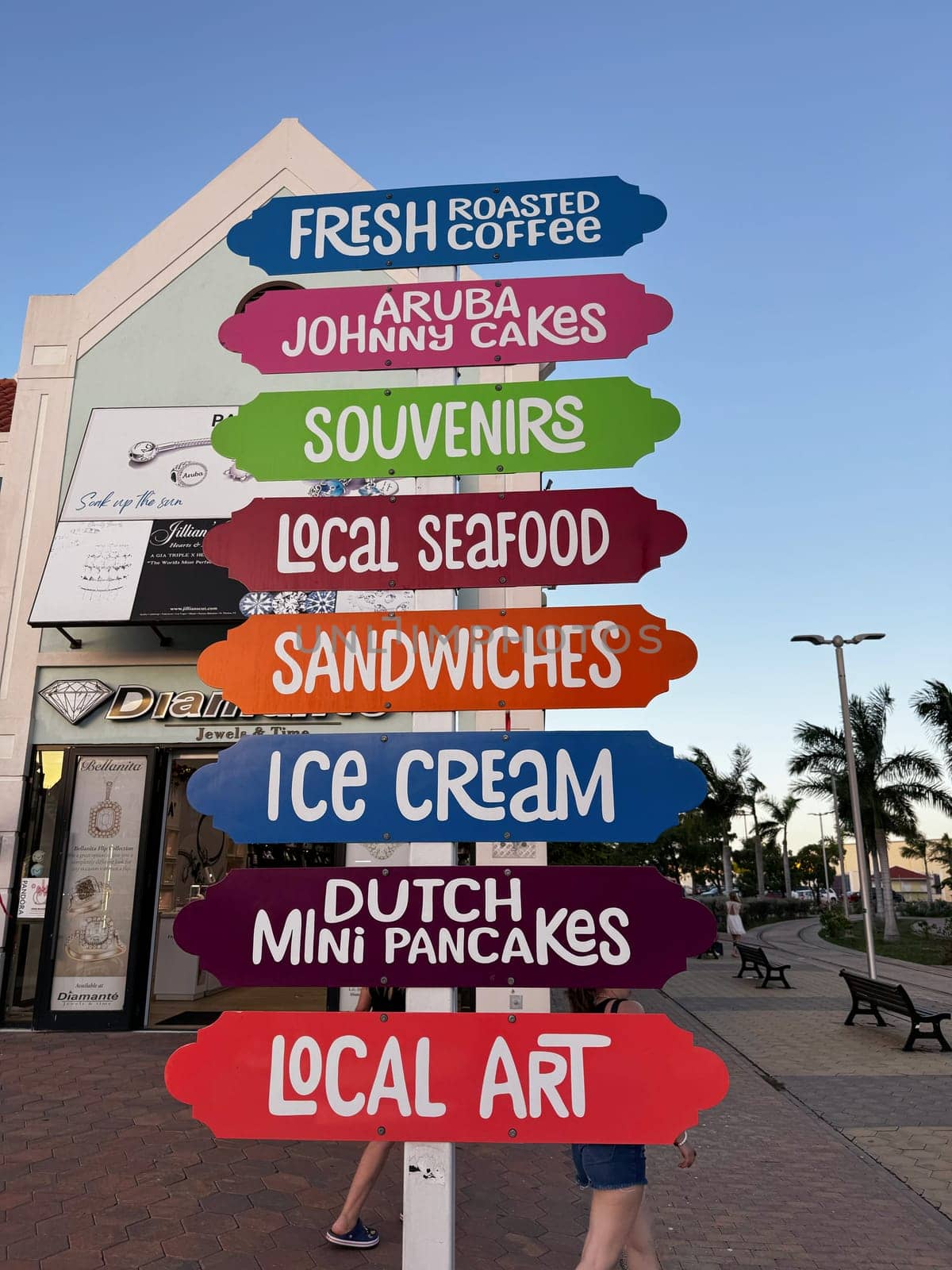 Holland, Aruba 11.22.2023 Vibrant wooden signpost in Aruba lists local foods, drinks, and souvenirs like Johnny cakes, Dutch pancakes, coffee, seafood, and art in a pedestrian-friendly shopping area.