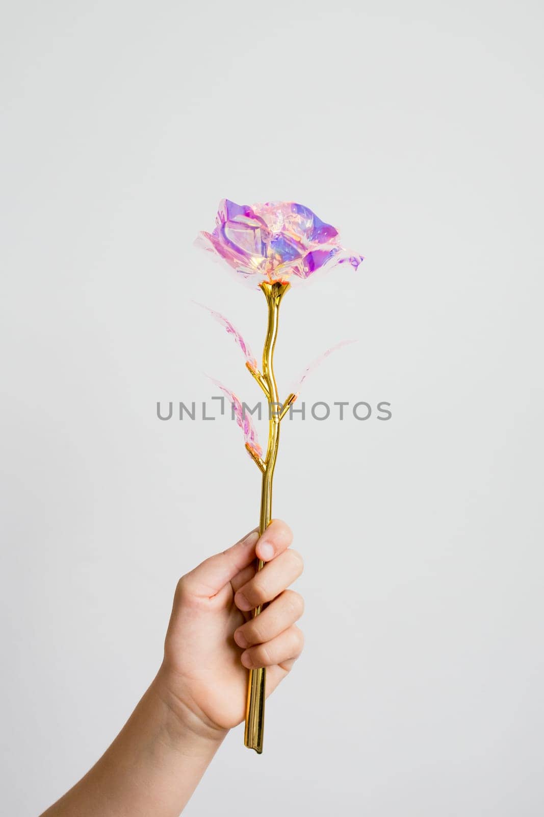Child hand holding decorative gold and purple rose against a soft background.