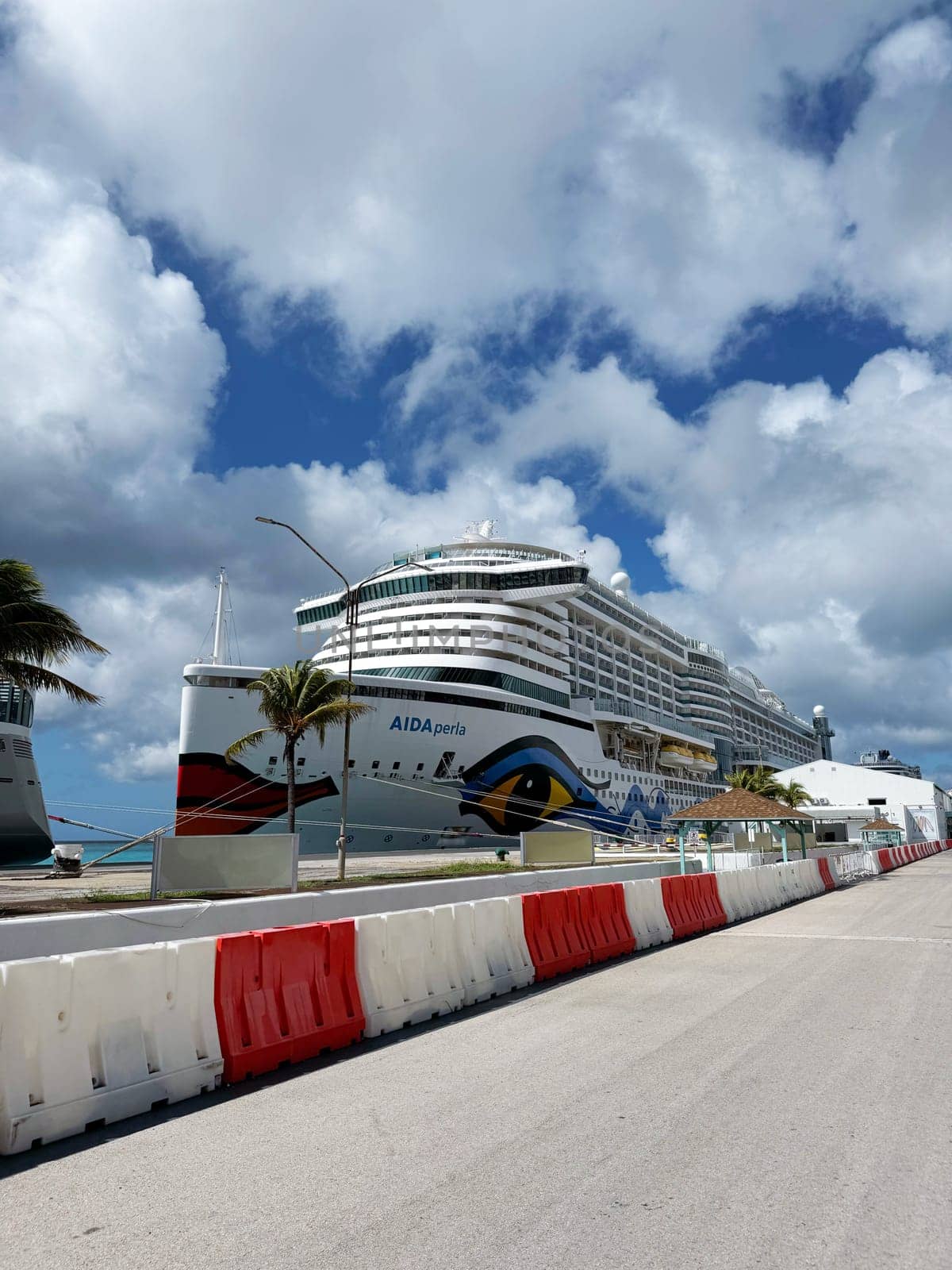 Bermuda, U.S. 10.22.2023 The AIDA Perla cruise ship is docked at a tropical Caribbean port under a partly cloudy sky. The scene shows palm trees, road barriers, and a calm atmosphere for tourists.