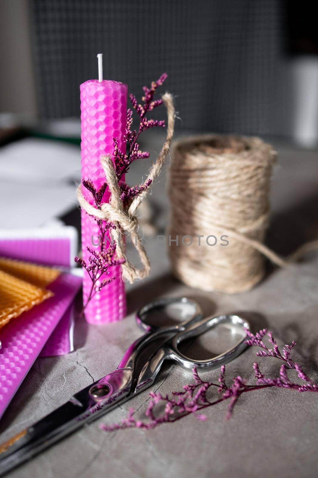 Pink beeswax candle with twine wreath on crafting table.