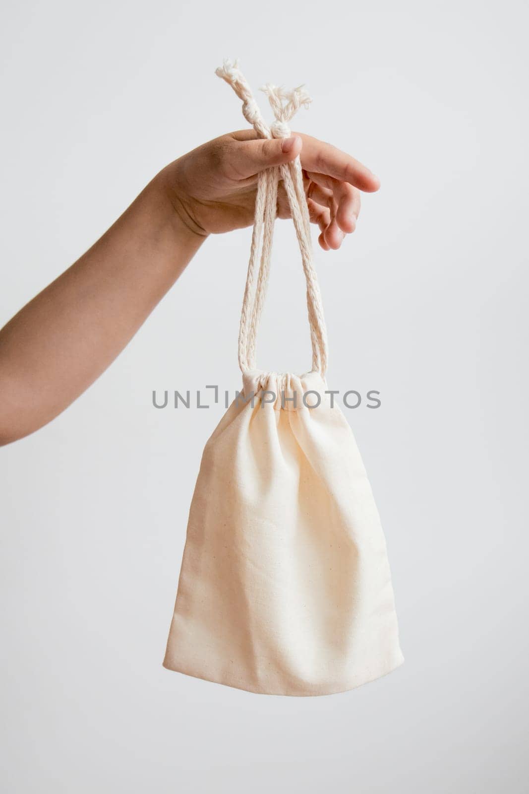 Hand holding cream cloth bag against white background.