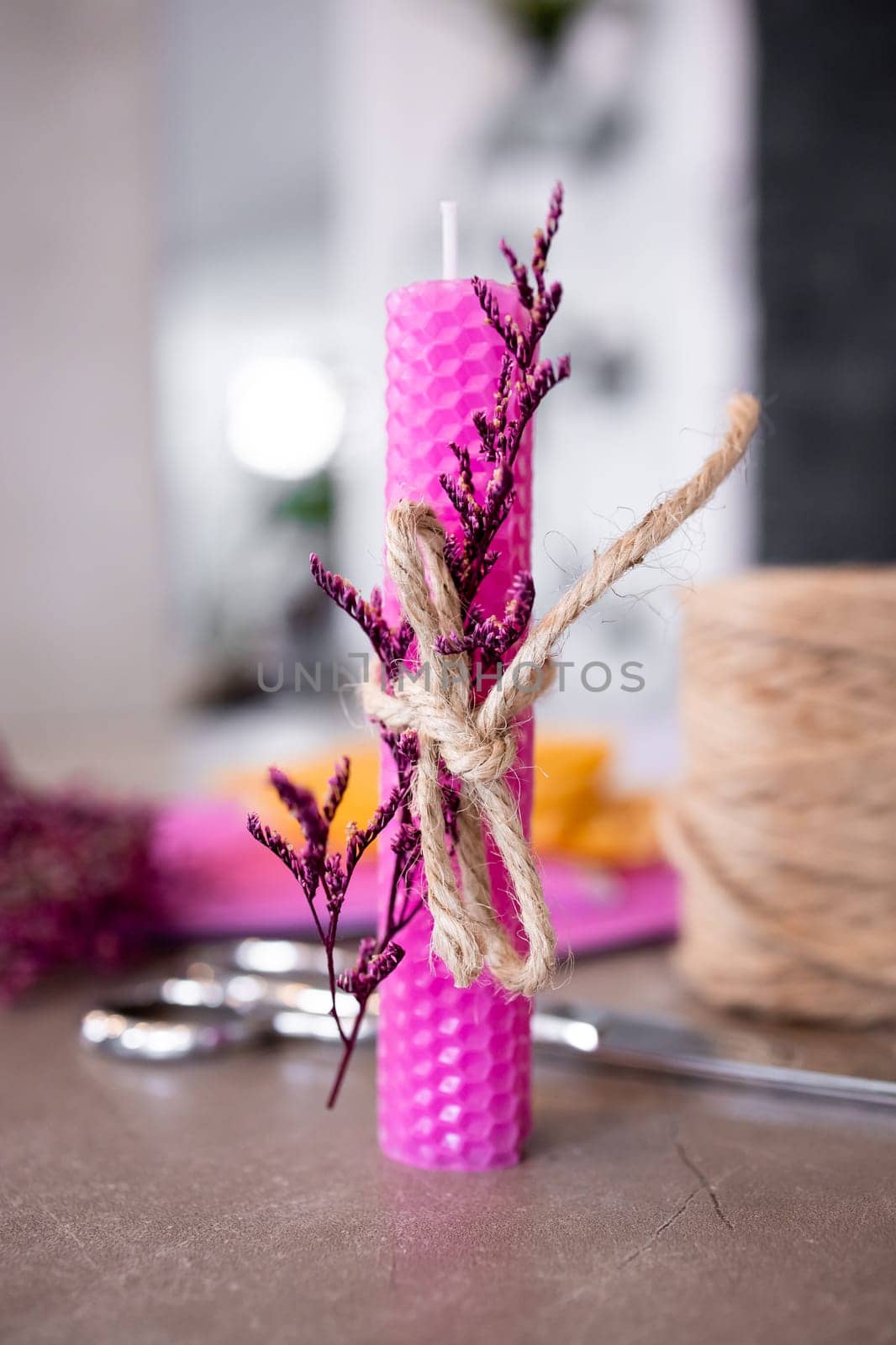 Pink textured candle with dried flowers and twine on table.
