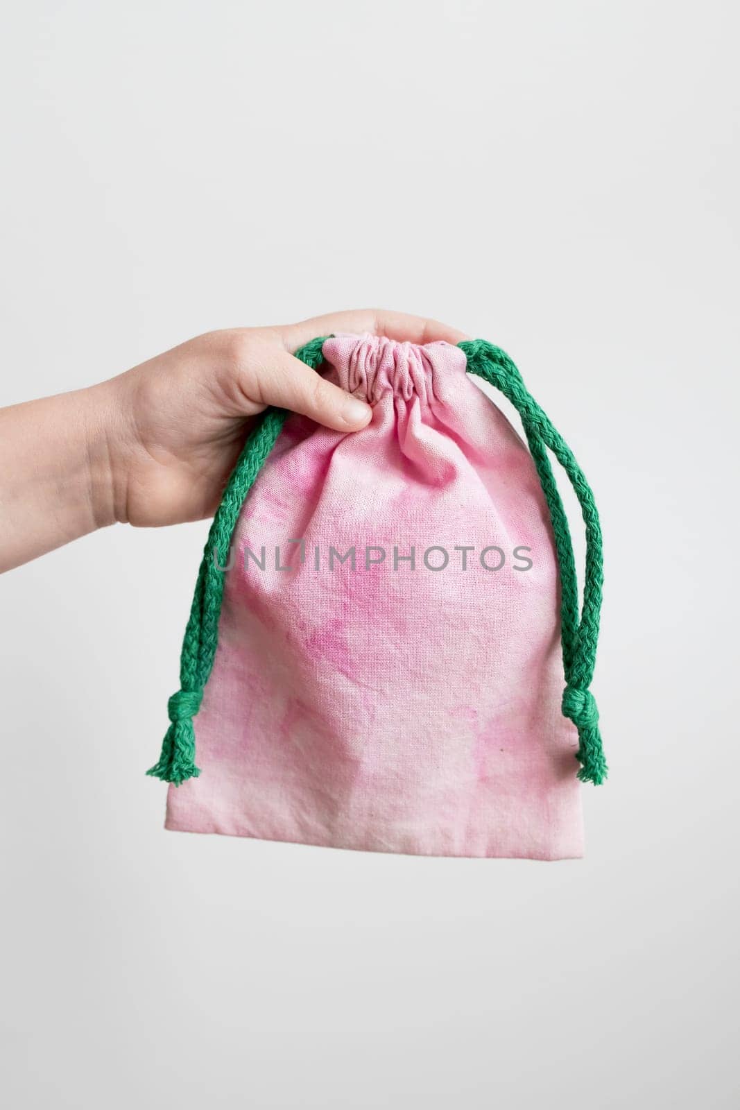 Hand holding pink drawstring bag with green rope against white background.