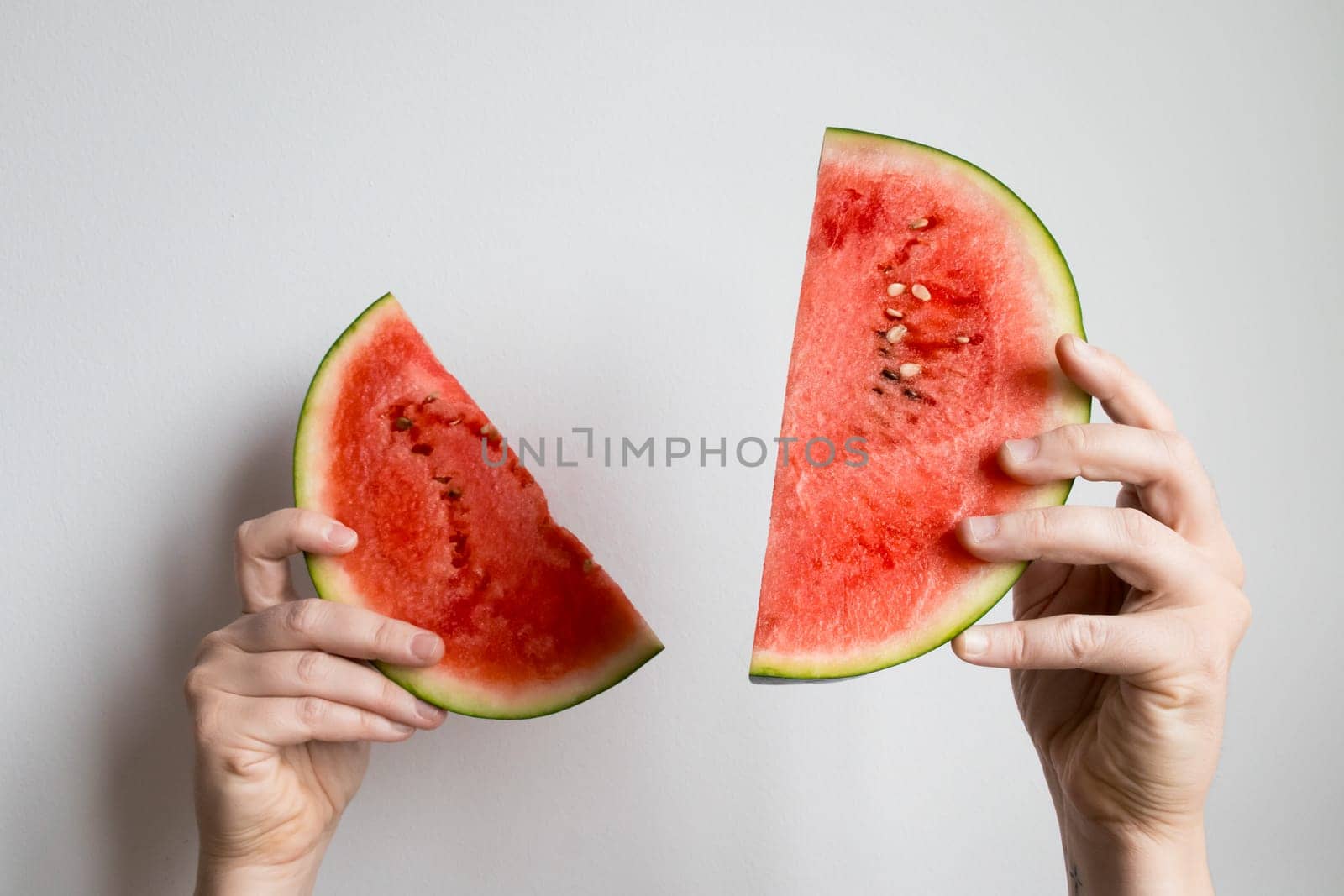 Hands holding sliced watermelon against white background.
