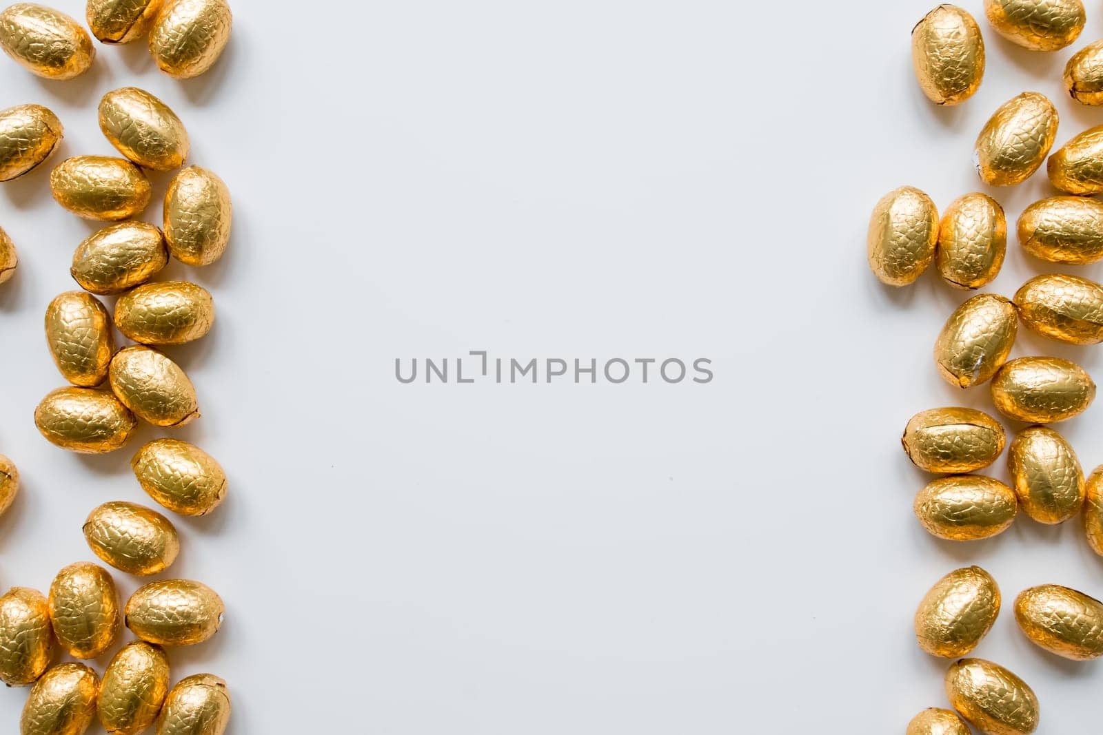 Golden foil wrapped chocolate eggs on white background with creative border.