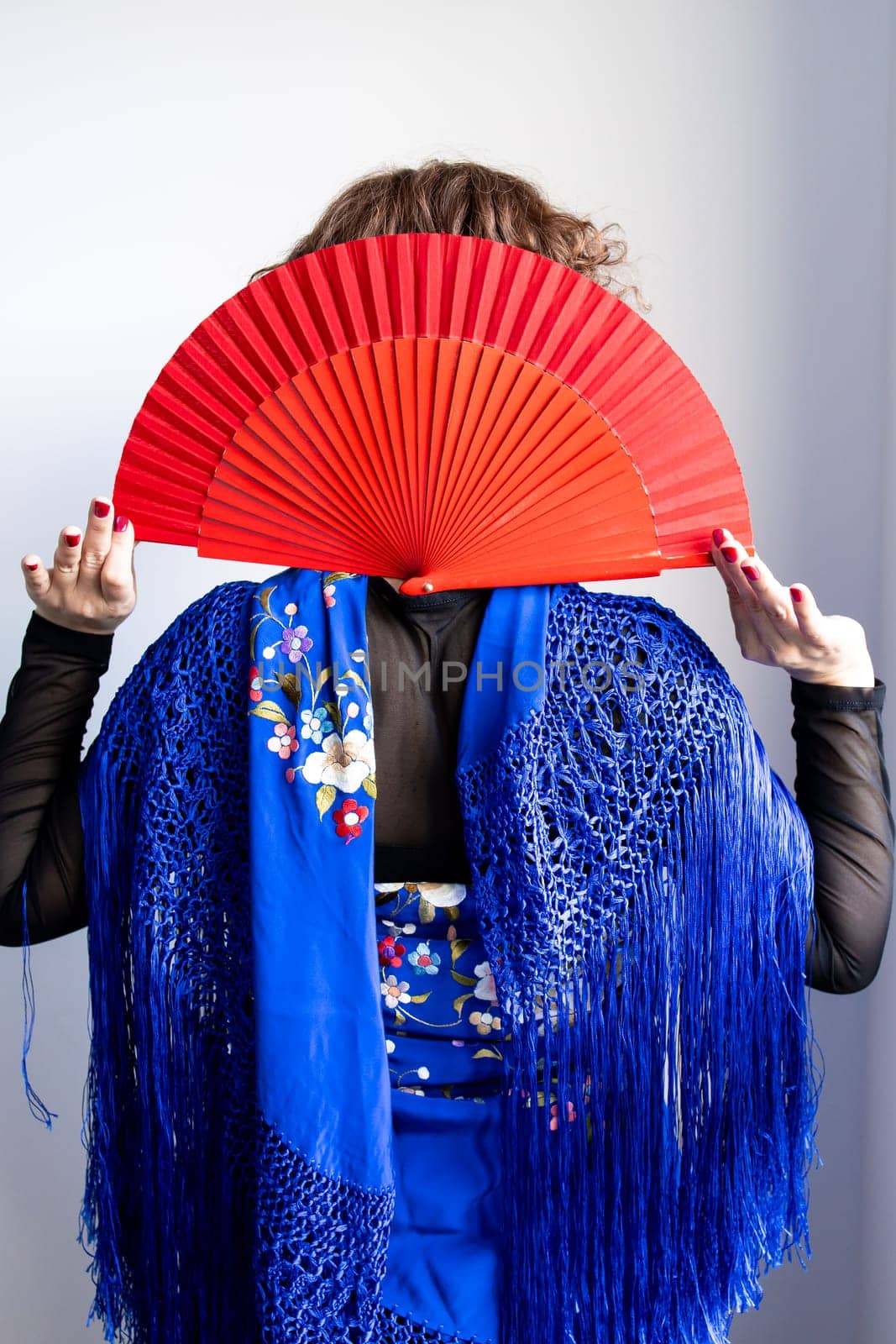 Hispanic female in traditional blue shawl holding red fan.