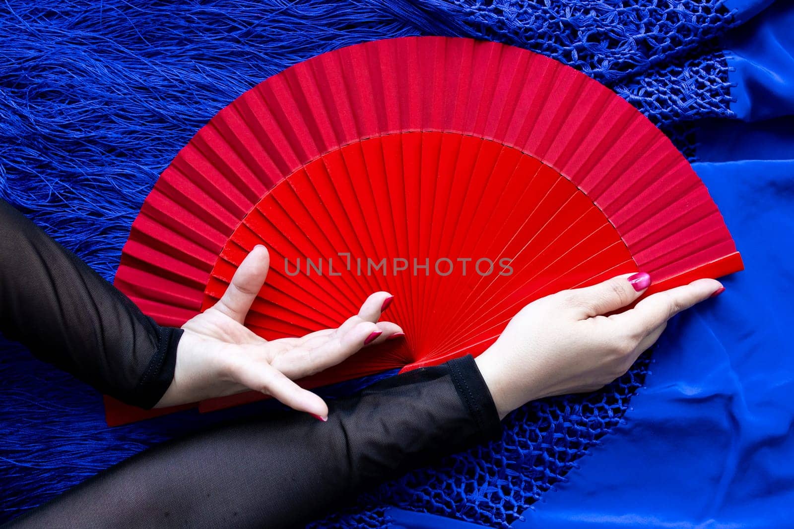 Elegant hand holding red fan on blue fabric background.