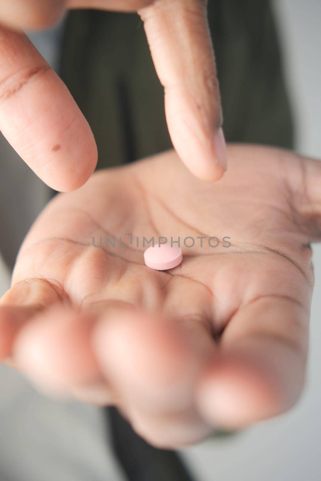 Someone gently pinches a pink tablet in their hand, considering its use.
