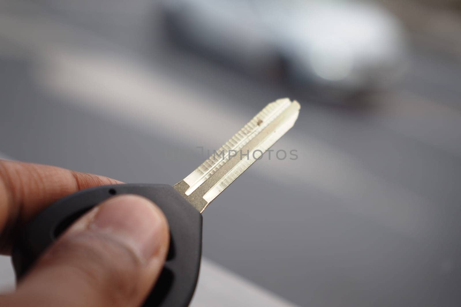 Hand grips a car key with a blurred vehicle in motion nearby.