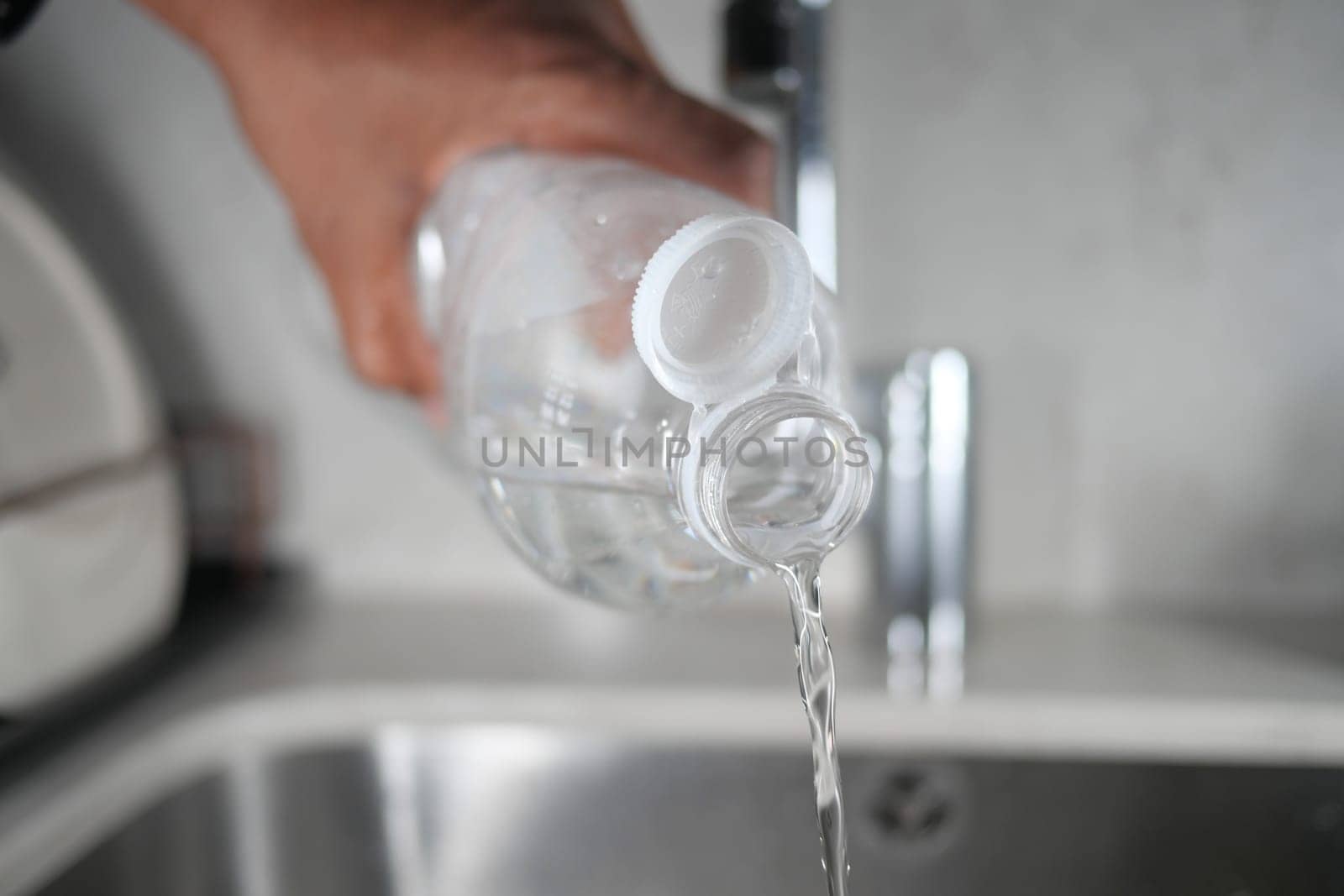 Person pours clean water from a bottle into a kitchen sink.
