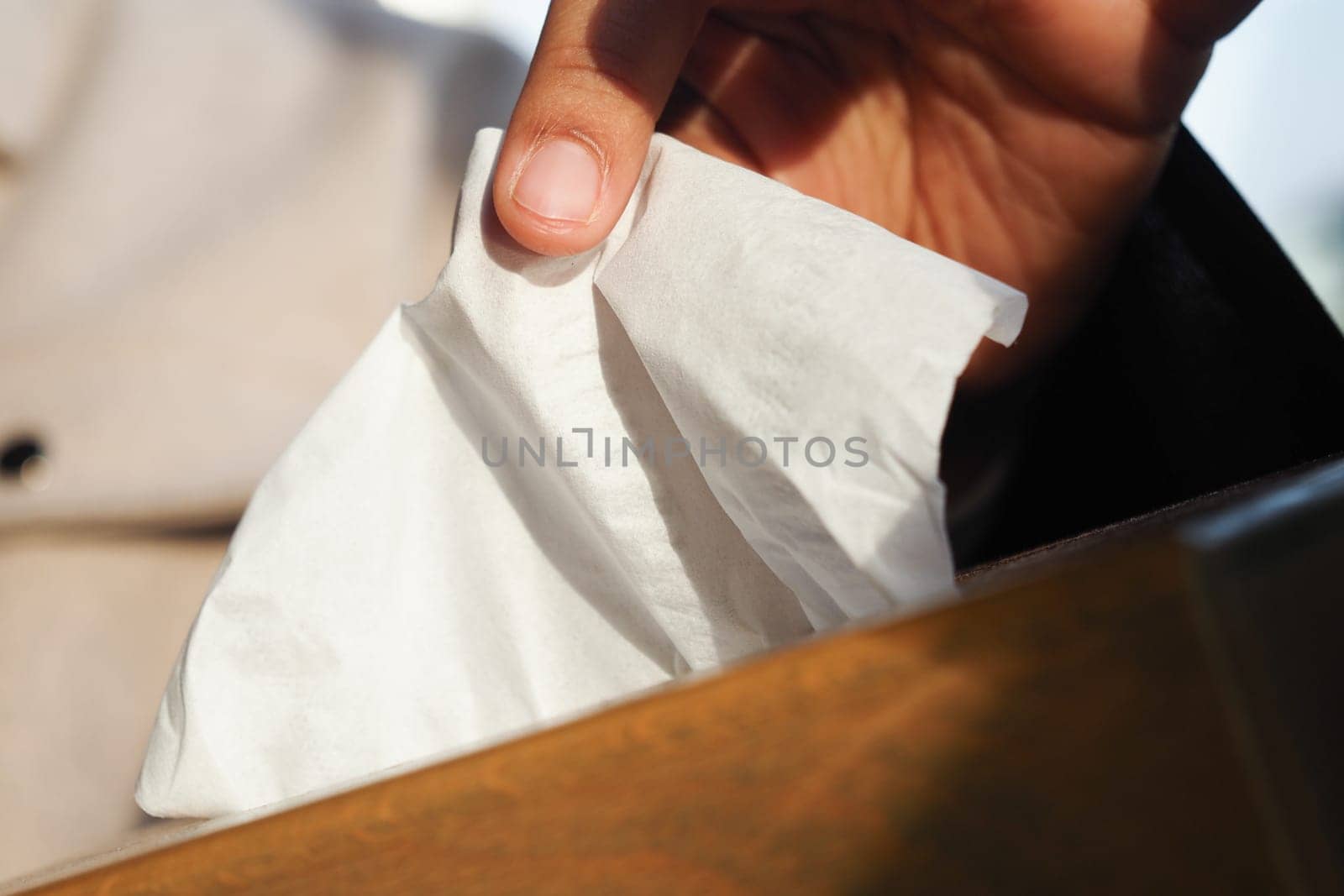 Close view of a hand selecting a tissue from a wooden box outdoors in sunlight.