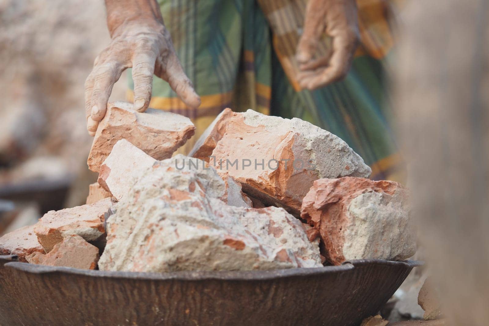 A person skillfully picks up clay bricks from a metal dish while working.