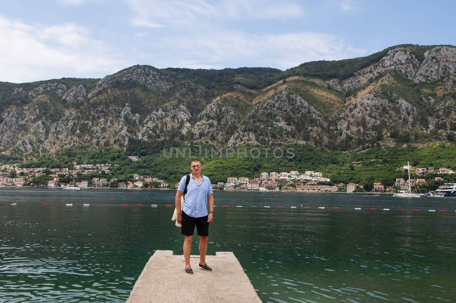 A man enjoys a scenic view of a bay and mountains, standing on a small pier.