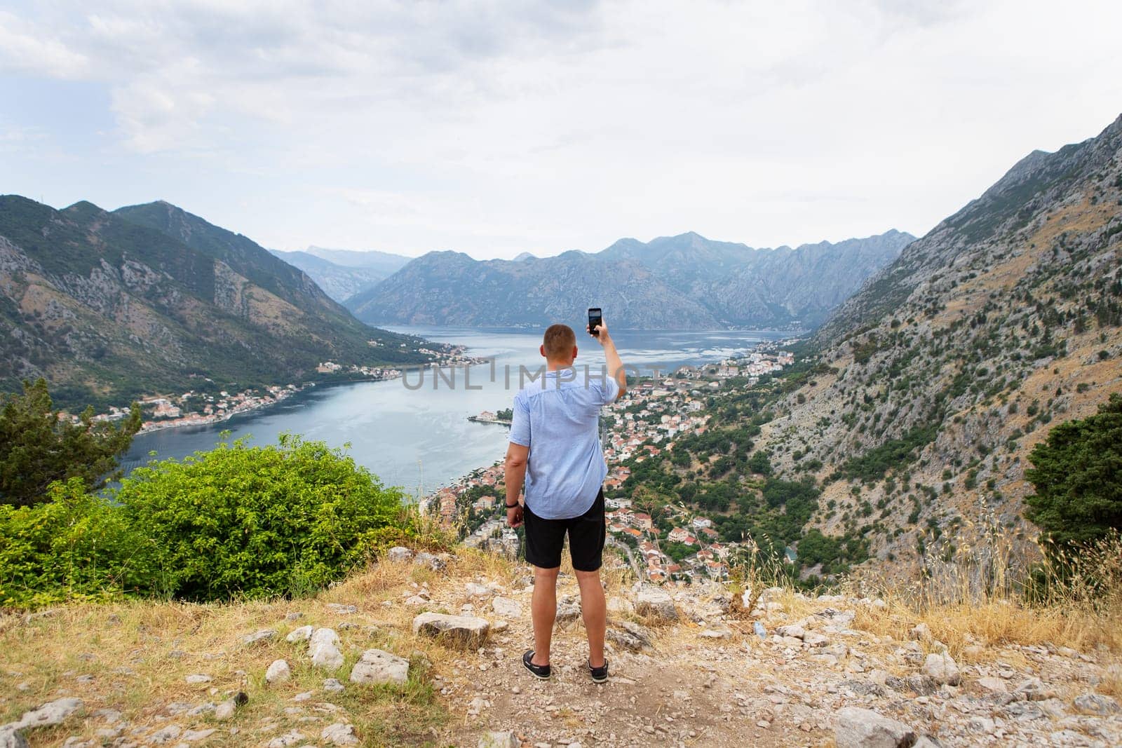 A man takes a photo of a stunning bay view from a mountaintop, capturing the picturesque landscape with his phone.