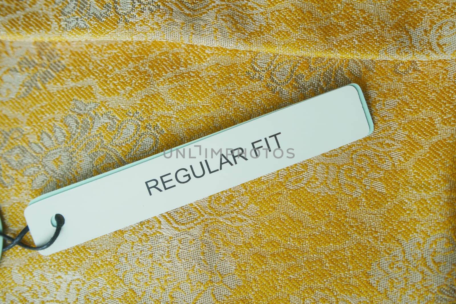 A tag labeled regular fit rests on textured yellow fabric showing design.