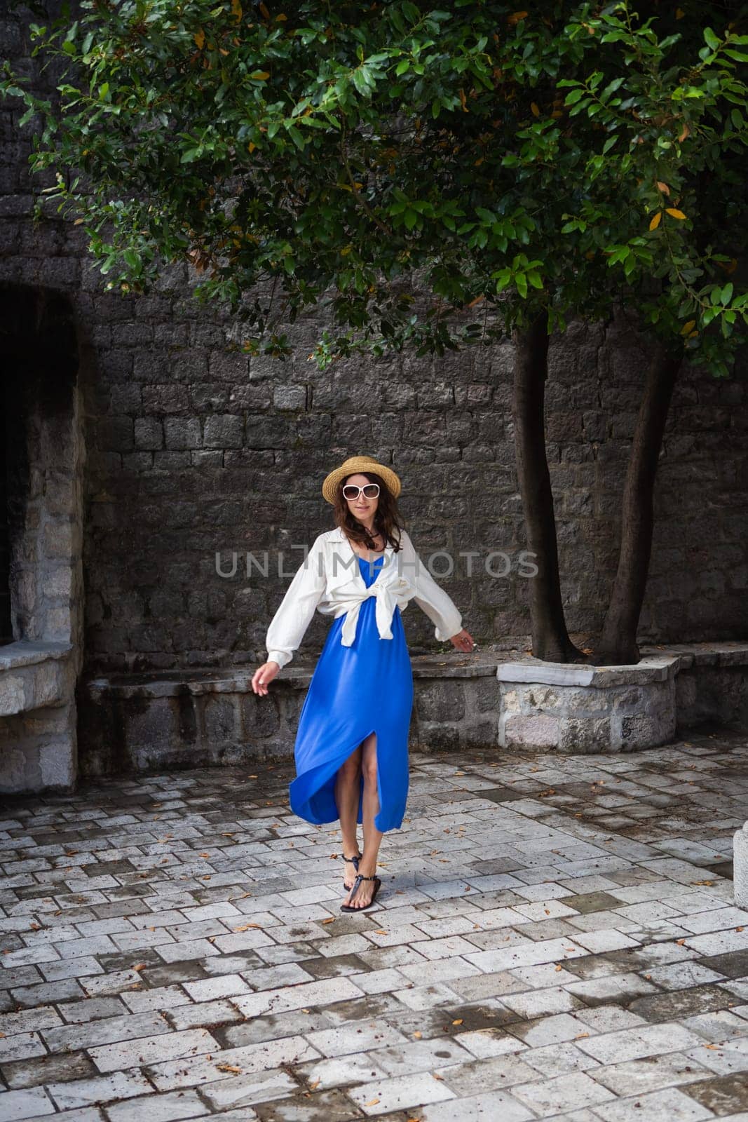 A girl in a blue dress and a straw hat walks through the old town of Europe