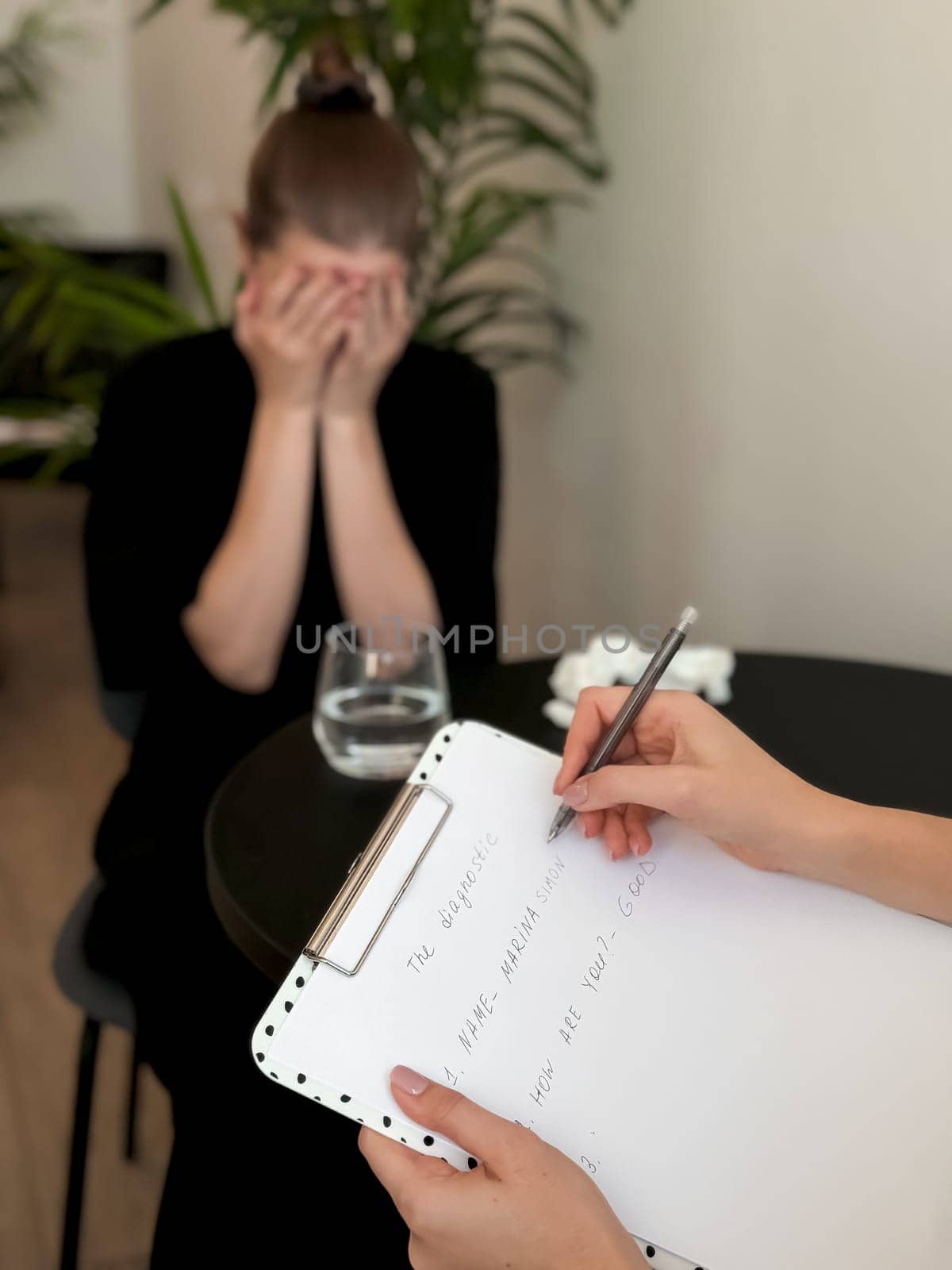 Stressed female adult in therapy session with therapist taking notes.