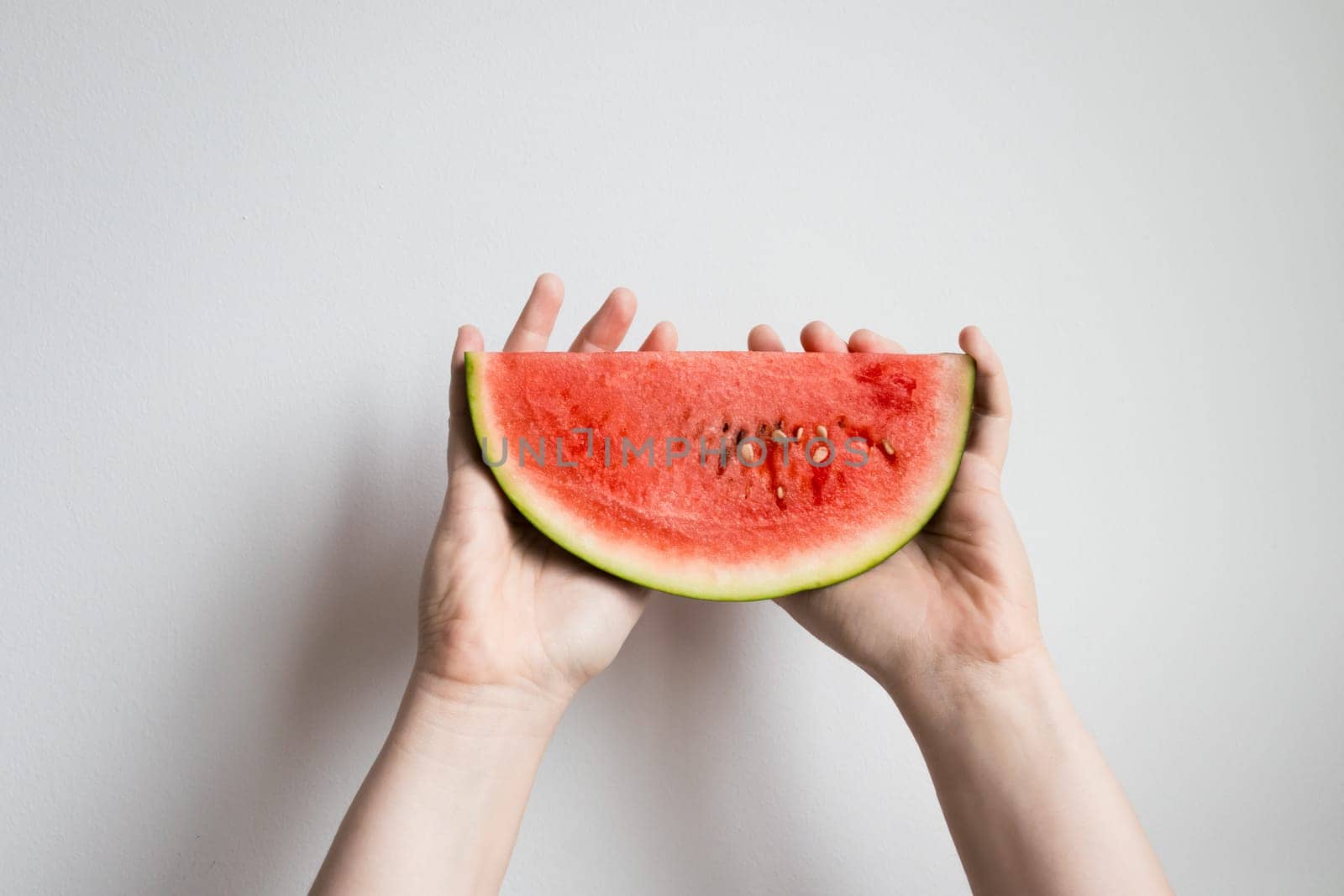 Hands holding juicy watermelon slice against white background.