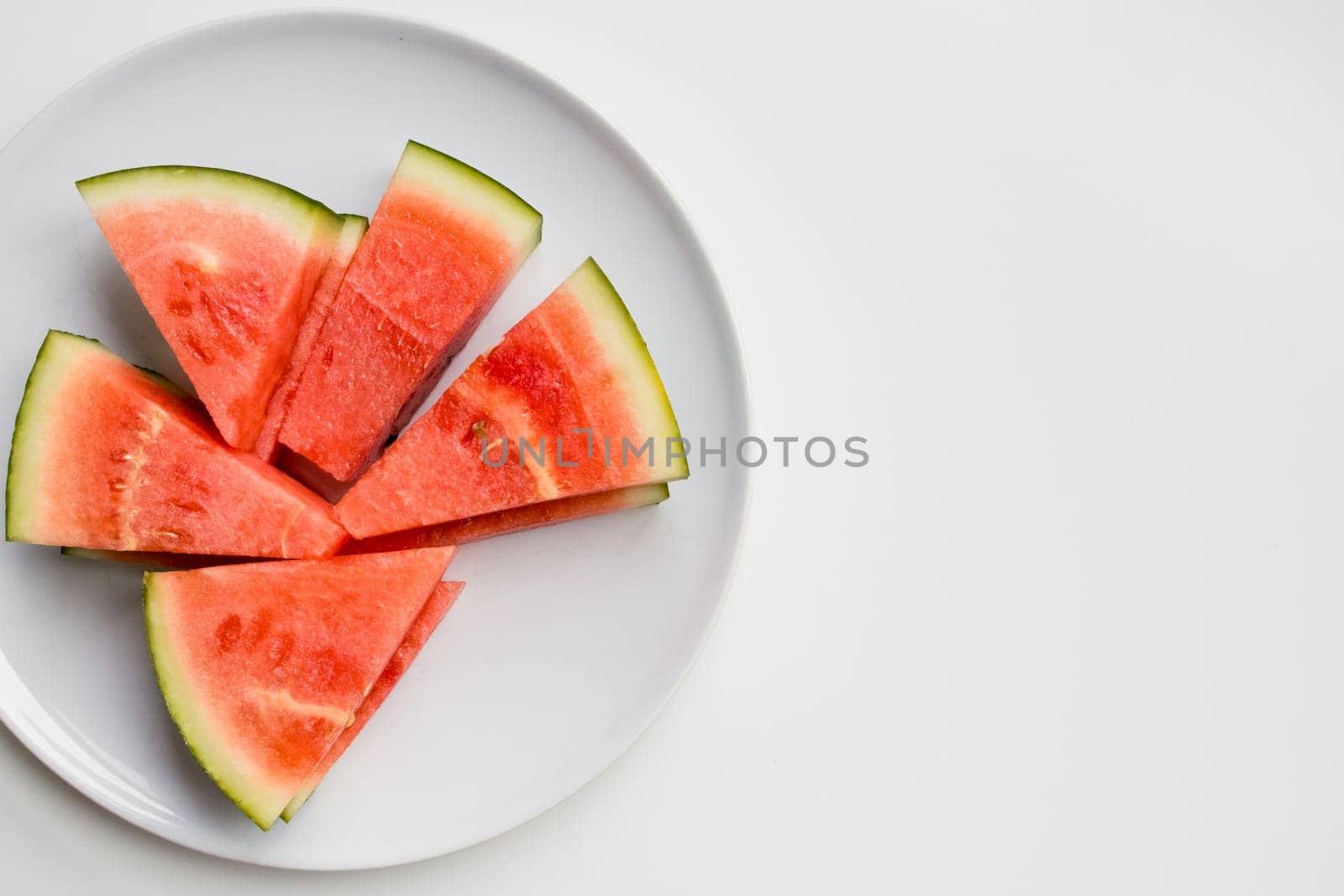 Fresh watermelon slices on white plate against minimalist background.