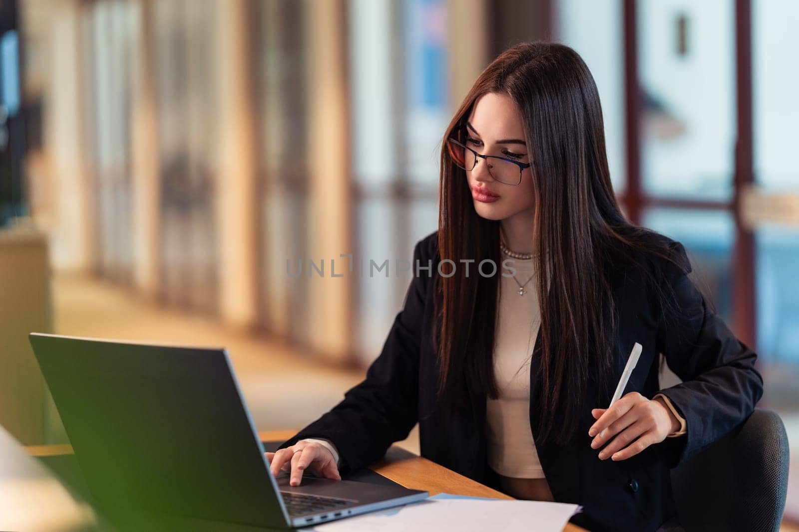 Focused, driven, unstoppable. A professional woman works on her laptop in a modern office, tackling tasks with confidence. Productivity and ambition in a fast-paced work environment.