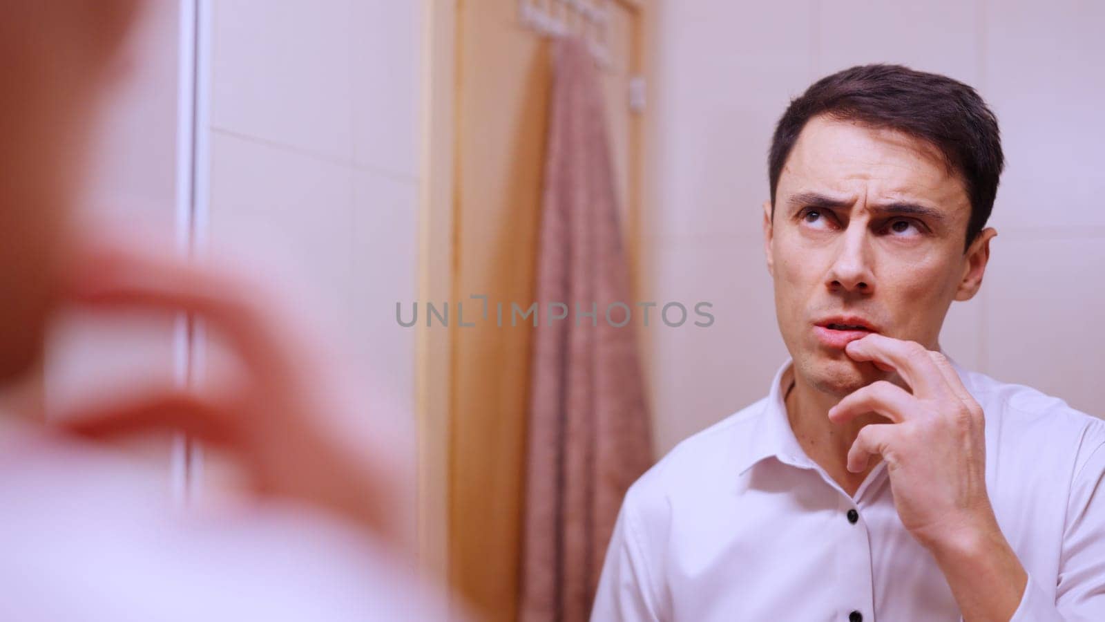 Businessman looking in the mirror with a pensive expression, touching his lips with his fingers