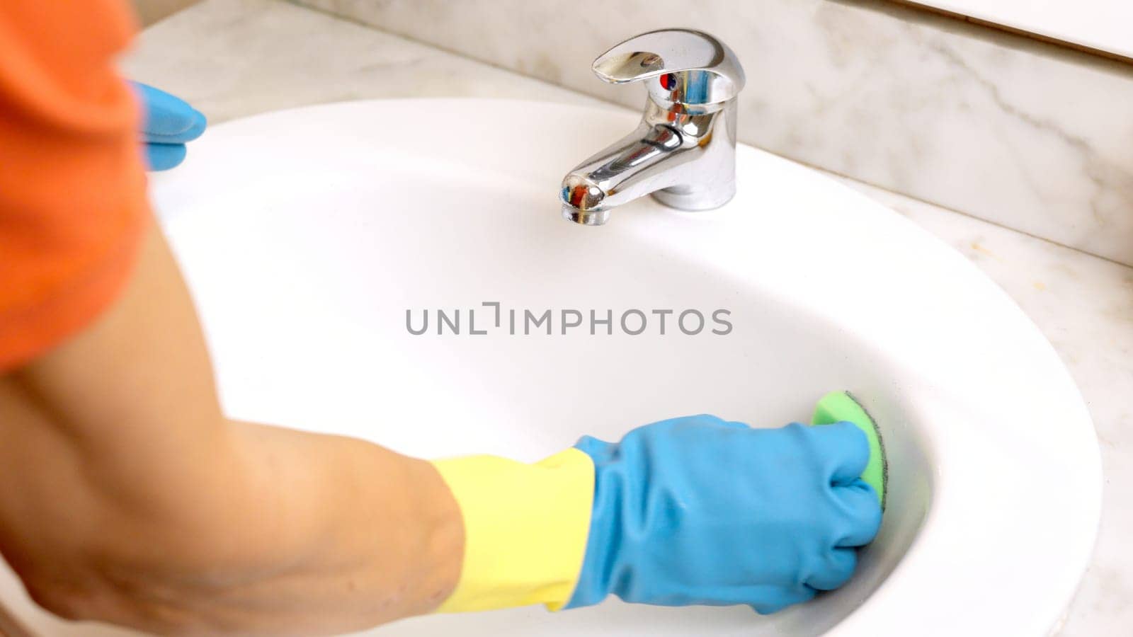 Janitor wearing gloves cleaning white sink with green sponge