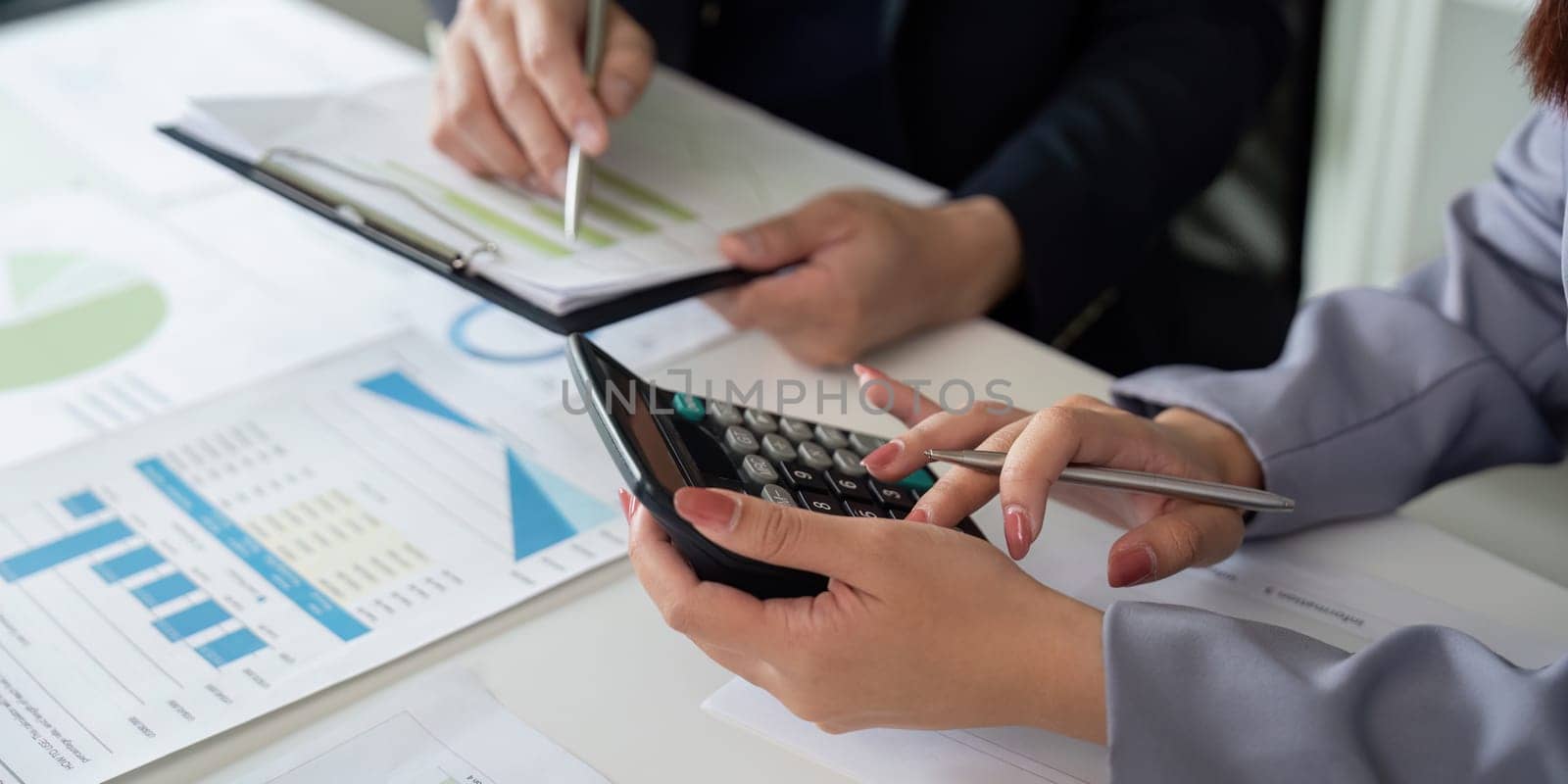 Two professionals analyze data together, one using a calculator to perform calculations, showcasing teamwork in financial analysis and reporting.