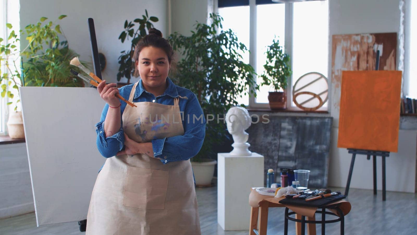 A woman painter posing with brushes in hand and looking in the camera. Mid shot