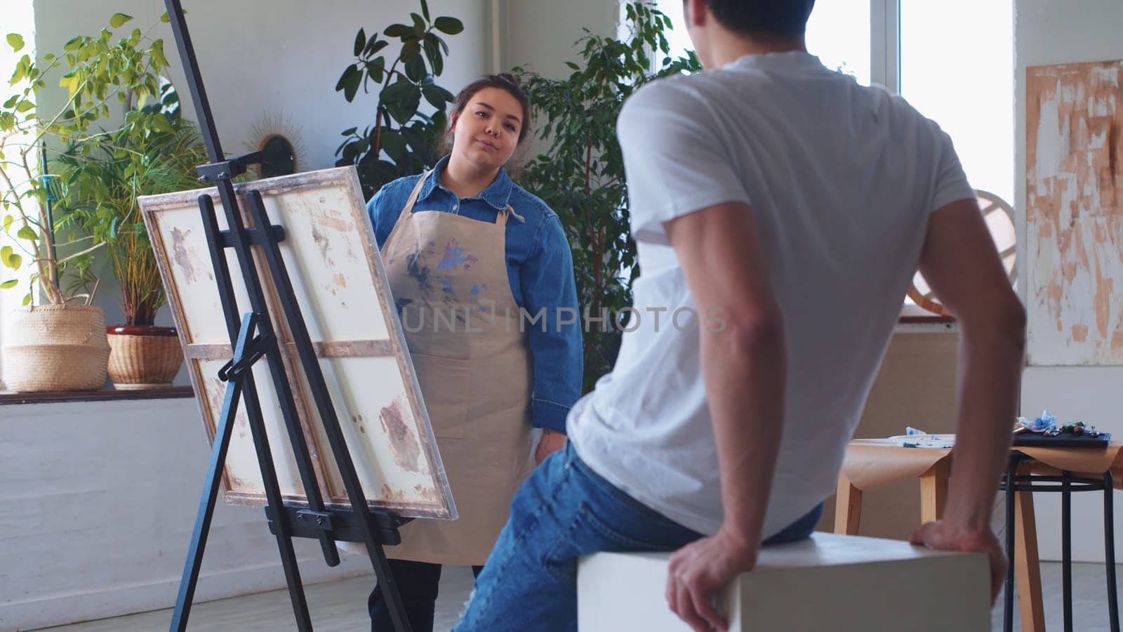 A woman paint artist drawing on a canvas taking a male model as a reference. Mid shot