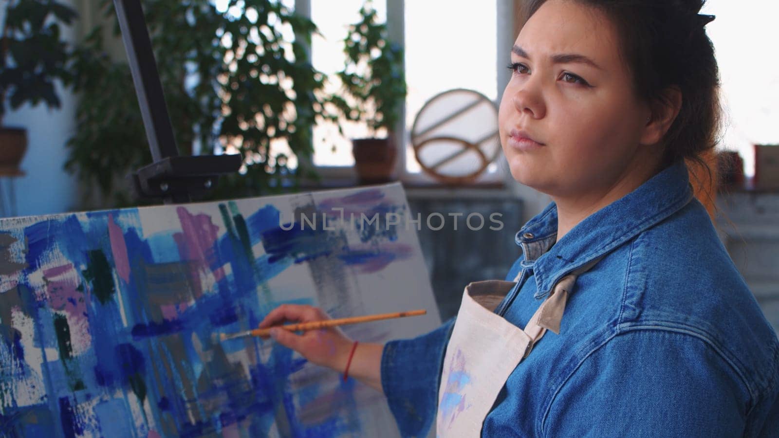 A woman artist drawing a painting and looking to the side. Mid shot