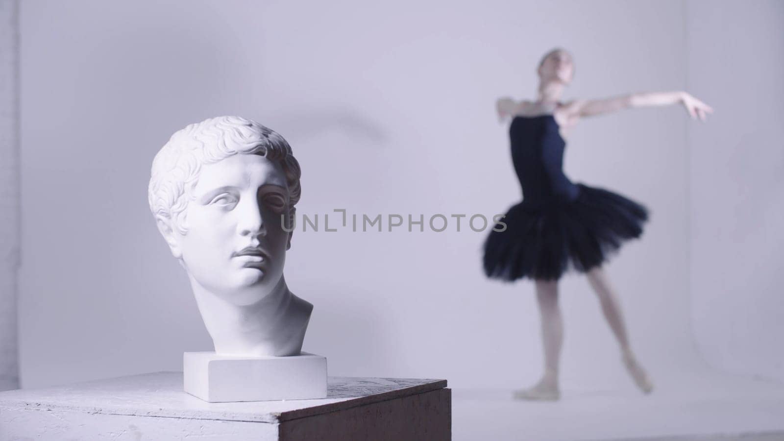 Young woman ballerina in black dress training - a head of greek sculpture on the foreground. Mid shot