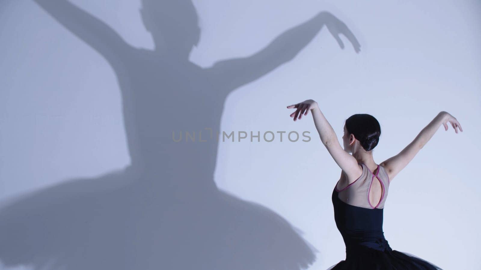 Young woman ballerina in black dress dancing - a big shadow on the wall. Mid shot