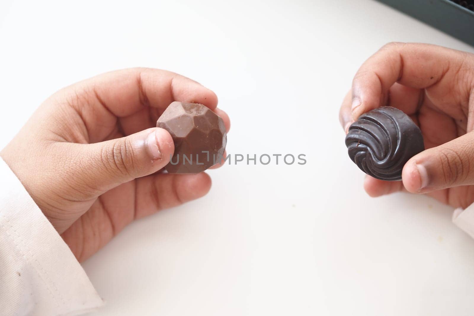 Two hands grasp unique chocolate pieces inside a bright indoor setting.